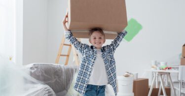 young boy smiling carrying moving box