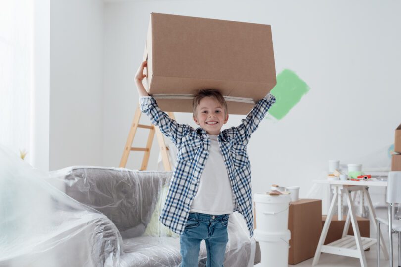 young boy smiling carrying moving box