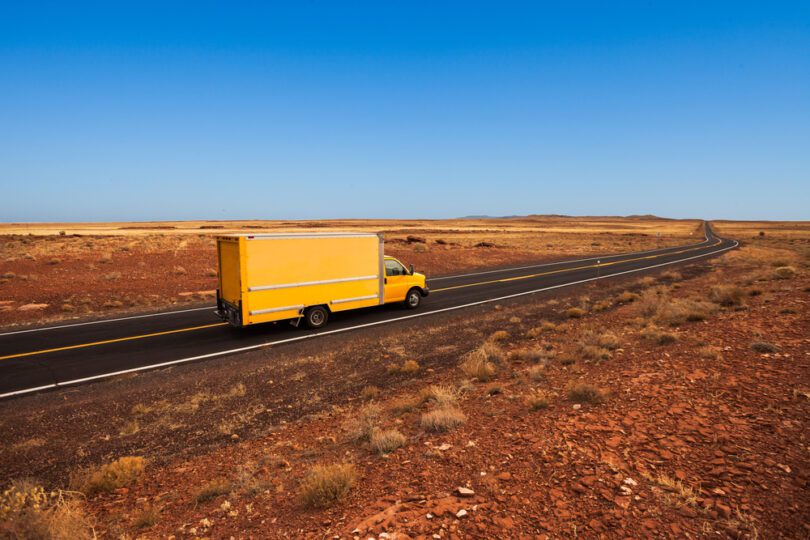 big yellow moving truck driving through the desert