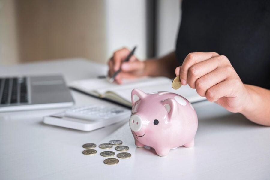 closeup of person with computer and notebook putting money in piggy bank