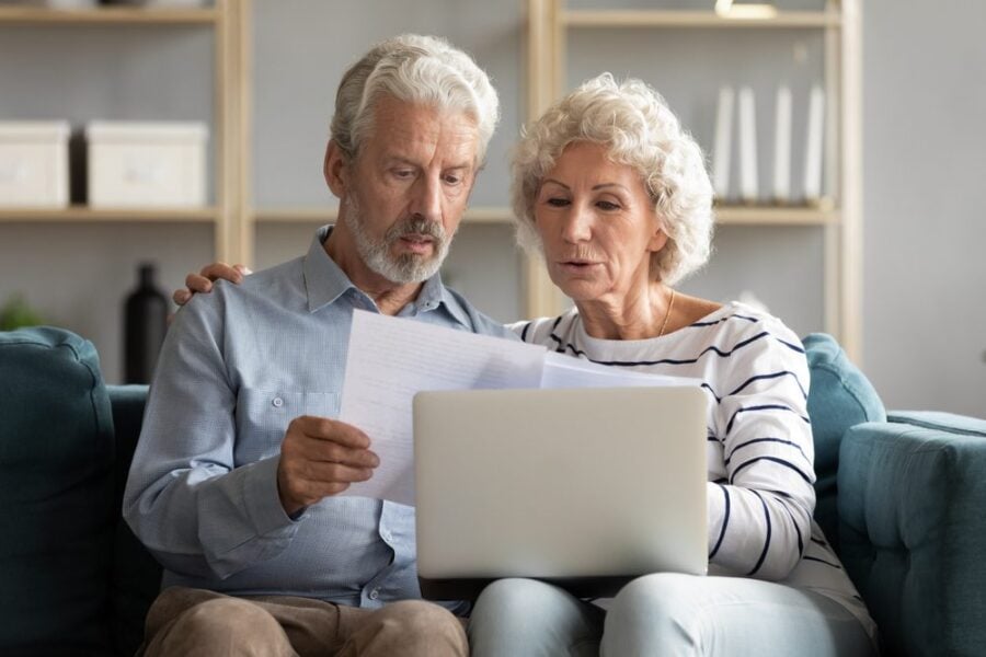 vibrant older couple on the sofa comparing moving quotes with papers and computer